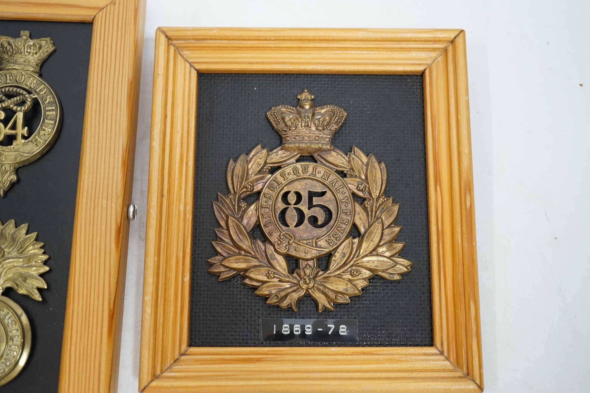 Five military helmet and shako plates mounted on two boards, including; the Nottinghamshire Regiment, the 2nd Staffordshire Regiment, the Royal Welsh Fusiliers, the Cumberland Regiment and the 85th King’s Light Infantry.